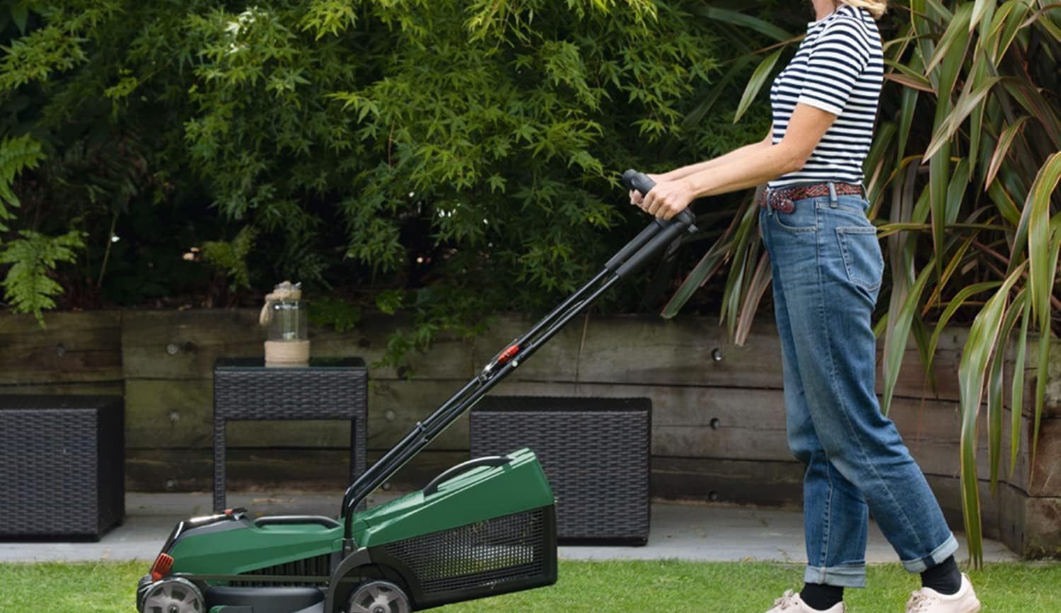 A cordless lawn mower being pushed across a green suburban lawn